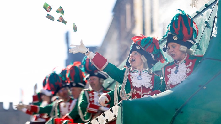 Karnevalisten auf einem Umzugswagen des Rosenmontagszugs 2025 auf der Kölner Severinstraße. Im Fokus des Bildes steht eine Frau, die gerade Kamelle in die Luft wirft.