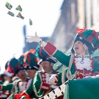 Karnevalisten auf einem Umzugswagen des Rosenmontagszugs 2025 auf der Kölner Severinstraße. Im Fokus des Bildes steht eine Frau, die gerade Kamelle in die Luft wirft.