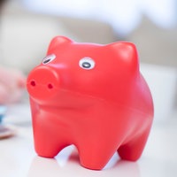 Ein Sparschwein und Geldscheine liegen auf einem Tisch vor einer Frau, die ihre Ausgaben notiert