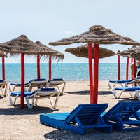 Liegestühle und Sonnenschirma an sonnigem Sandstrand mit Blick auf das Meer mit klarem, türkisem Wasser.