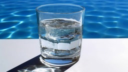 Ein mit Wasser gefülltes Glas am Rand eines Pools