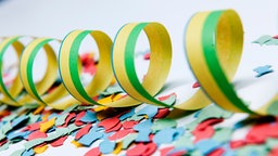 Gelb-grüne Luftschlangen und buntes Konfetti liegen auf einer weißen Oberfläche