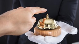 Eine Person betätigt die Serviceklingel, die von einem Kellner mit weißen Handschuhen gehalten wird.