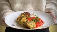 Ein angerichteter Teller mit gebratenen Bärlauchknödeln und Tomatensauce wird in die Kamera gehalten.