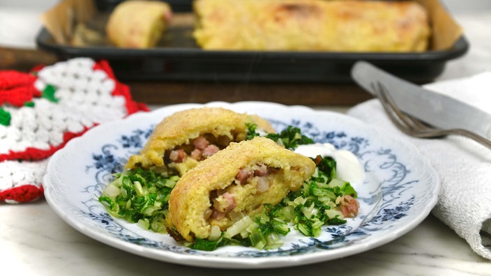 Eine aufgeschnittene Kartoffelroulade wird mit Rübenstiel auf einem Teller serviert.