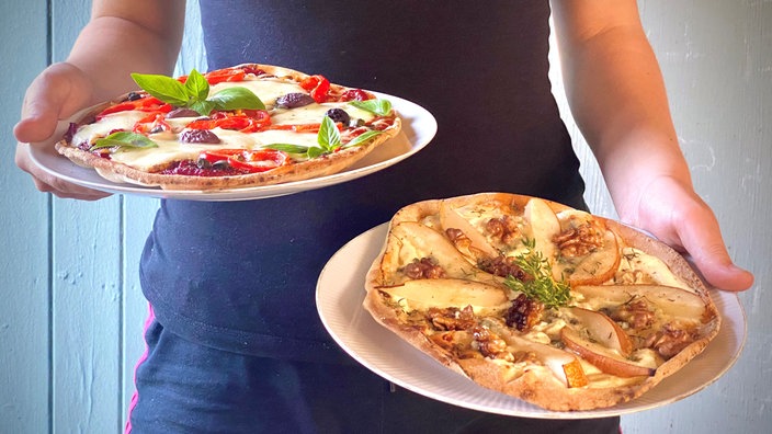 Zwei Teller mit orientalischem Pfannenbrot werden in die Kamera gehalten, einmal als Pizza und einmal als Flammkuchen