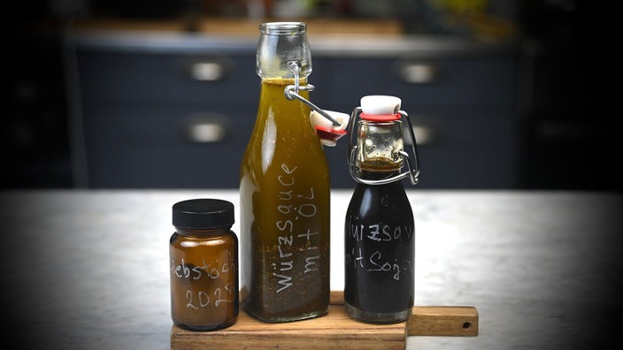 Drei Gefäße mit selbst gemachter Würzsauce stehen auf einem Holzbrett