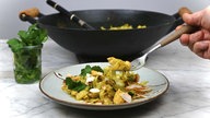Spitzkohl und Hähnchen in Curry-Kokos-Sauce ist auf einem Teller angerichtet, im Hintergrund stehen ein Glas mit frischem Koriander und das restliche Curry in einer Wok-Pfanne