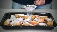 Apfelringe auf einem schwarzen Blech, die gerade mit Puderzucker bestreut werden.