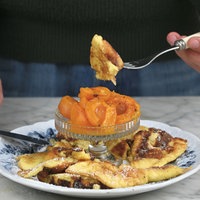Ein Teller mit Kaiserschmarrn und einem Schälchen geröstete Aprikosen. Es wird gerade ein Stück Kaiserschmarrn mit einer Gabel vom Teller gehoben. 