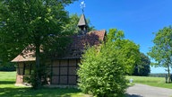 Durch die Baumberge: Alte Kapelle mit Fachwerk und Türmchen eingebettet in Wald und Wiese unter blauem Himmel