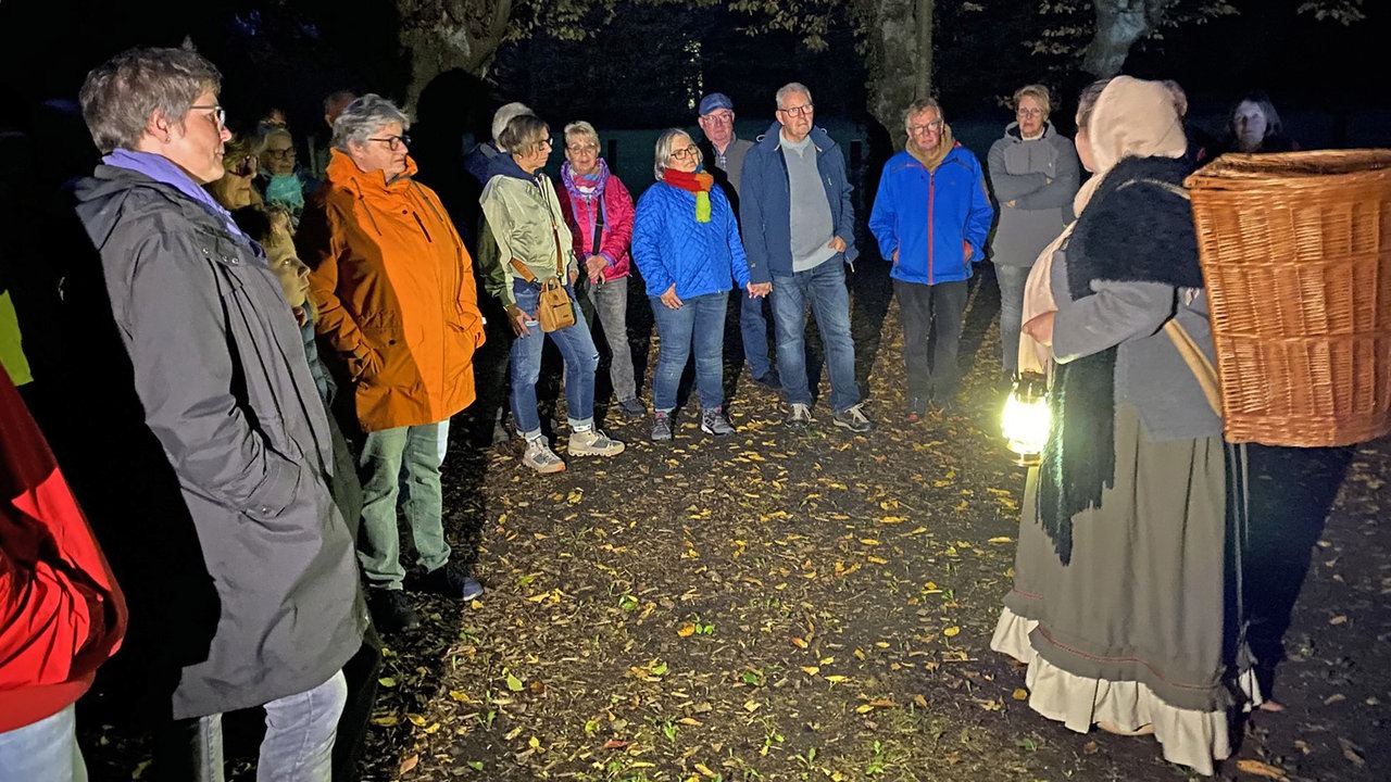 Eine verkleidete Darstellerin mit Laterne und die Teilnehmer der Wanderung im Dunkeln. 