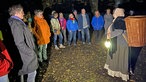 Eine verkleidete Darstellerin mit Laterne und die Teilnehmer der Wanderung im Dunkeln. 