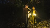 Zwei verkleidete Darsteller mit Laternen im dunklen Wald.
