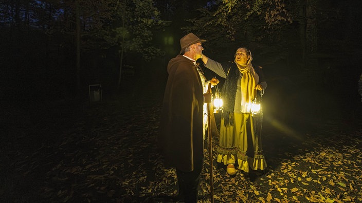 Zwei verkleidete Darsteller mit Laternen im dunklen Wald.