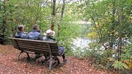 Drei Personen von hinten sichtbar auf einer Bank sizend mit Blick auf die Glörtalsperre
