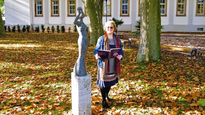 Stadtführerin vor einer Bronzefigur: Sie begleitet die Wanderungen mit ihrem Märchenbuch.