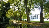Blick in den Kurpark mit kleinem See im Vordergrund und der Kaiserpalais von Bad Oeynhausen im Hintergrund