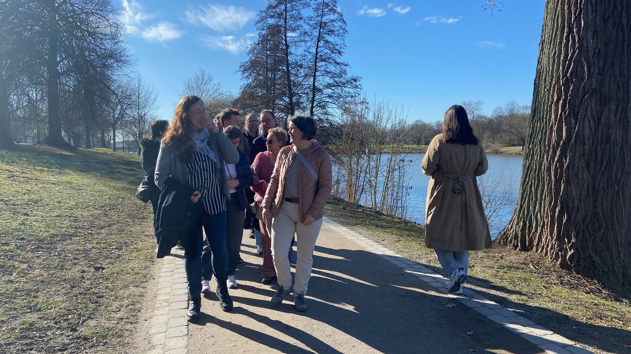 Eine Gruppe Spaziergänger auf einem Fußweg am Aasee an einem sonnigen Tag.