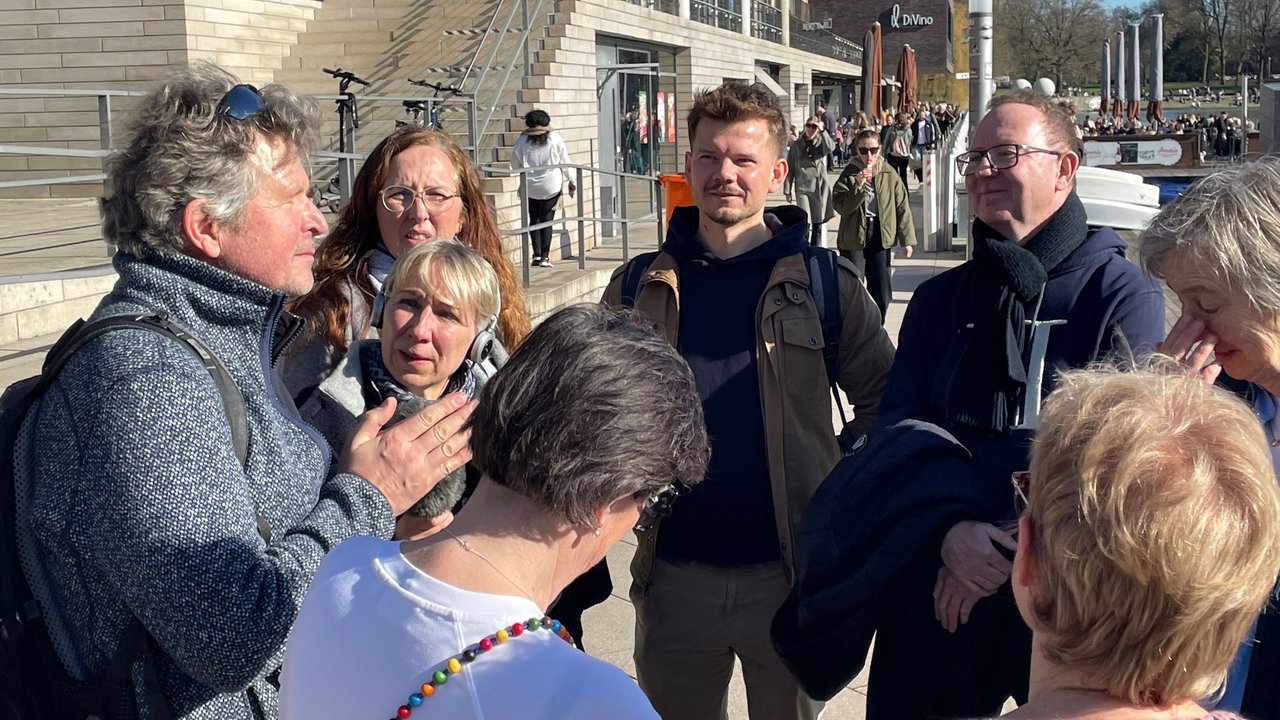 Eine Gruppe der Teilnehmer von "Ideen im Gehen" stehen im Kreis. Links im Bild steht Anleiter Bertold Raschkowski. Die Teilnehmenden schauen Ihn an. 
