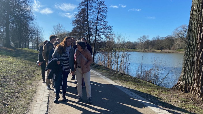 Die Teilnehmer von "Ideen im Gehen" auf einem Fußweg. Alle sind sichtlich in Gesprächen mit ihren Mitspazierenden. Rechts im Bild ist der Aasee zu sehen.
