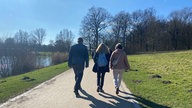 Drei Süaziergänger von hinten fotografiert. Links im Bild ist der Aasee zu sehen. 