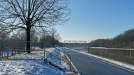 Ein Gehweg neben dem Kanal: Am linken Bildrand befindet sich eine Treppe, die vom Kanal wegführt. Weiter hinten im Bild ist eine Brücke über den Kanal zu sehen.