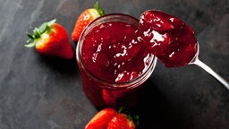 Erdbeerkonfitüre in einem Glas mit einem Löffel, im Hintergrund Erdbeeren