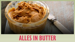 Gläschen mit Erdnussbutter und Messer mit "Alles in Butter"-Banner 