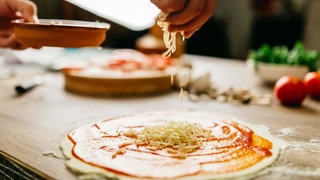 Pizzateig mit Tomantensauce wird mit Käse bestreut. 
