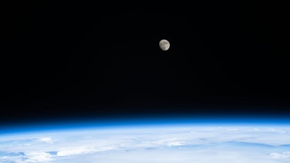 Blick von der ISS auf den Mond, darunter leuchtet blau die Erde