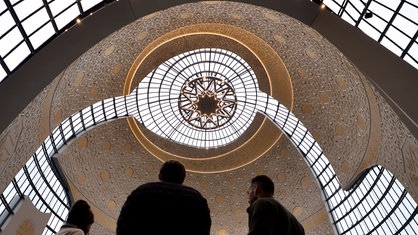 Menschen stehen mit dem Rücken zur Kamera in der Zentralmoschee in Köln, über ihnen spannt sich die weite Kuppel 