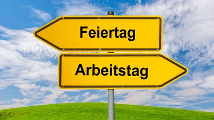Zwei Wegweiser zeigen in unterschiedliche Richtungen, auf dem einen steht Feiertag, auf dem anderen Arbeitstag geschrieben