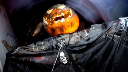 Ein Geist mit Kürbiskopf steht zu Halloween im Vorgarten eines Hauses 