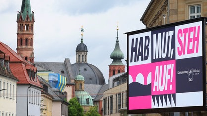 Der Slogan "HAB MUT, STEH AUF!" ist auf dem Residenzplatz vor den Türmen des Kiliansdoms und der Neumünsterkirche zu sehen.