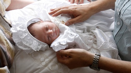 Ein Baby mit Davidsstern um den Hals liegt vor der Beschneidung ruhig in den Armen seiner Eltern