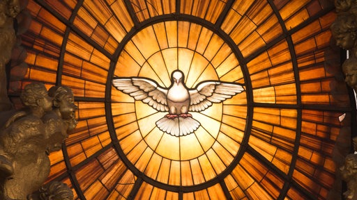 Ein Fenster mit einer Heilig-Geist-Darstellung im Form einer weißen Taube leuchtet im Petersdom im Vatikan während einer Messe
