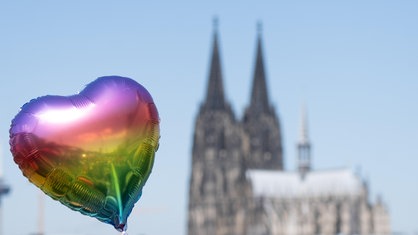 Ein herzförmiger Luftballon in Regenbogenfarben beim CSD 2022 - im Hintergrund ist der Kölner Dom zu sehen