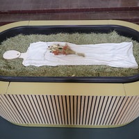 Heu, Stroh, Blumen und eine Holzfigur liegen in einem sogenannten Kokon für eine Reerdigung.