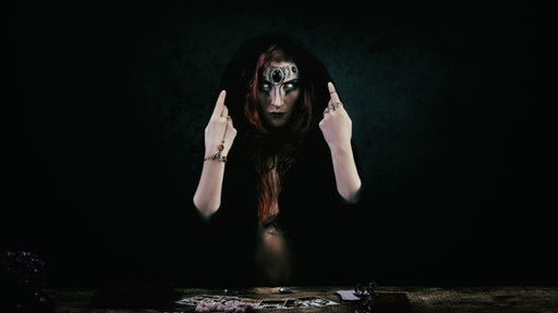 Eine düster verkleidete Hexe vor einem Tarotspiel
