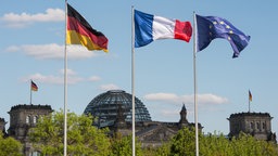 Fahnen von Deutschland, Frankreich und der Europäischen Union wehen im Wind mit dem Blick auf den Reichstag. 