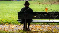 Rentnerin sitzt allein auf einer Parkbank