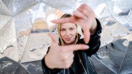 Junge Frau blickt lächelnd durch Rahmen aus ihren Fingern