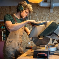 Ein Tischler steht mit Gehörschutz an seiner Kappsäge