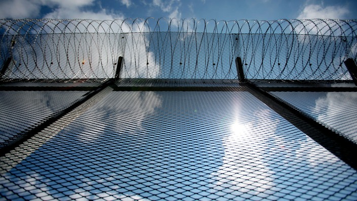 Der Zaun in der Justizvollzugsanstalt Wuppertal-Ronsdorf, dahinter ein blauer Sommerhimmel