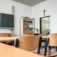 Tische und Stühle stehen in einem Klassenraum im Aloisiuskolleg in Bonn am 8. Juli 2019. Über der Tür hängt ein Kruzifix.