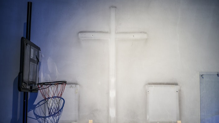Ein mobiler Basketballkorb steht vor dem Umriss eines abgehängten Kreuzes an einer Wand in der entweihten katholische Kirche St. Josef in Gelsenkirchen-Ueckendorf im Rahmen der Kunstschau Manifesta 16 Ruhr.