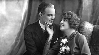 Schwarz-weiß-Fotografie um 1910 zeigt einen Mann und eine Frau, die nebeneinander sitzen und flirten