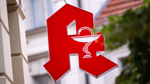 Ein rotes Apotheken-Symbol ist außen an einer Hauswand angebracht.