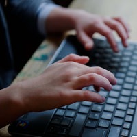 Nahaufnahme von Händen eines Mädchens, das auf der Tastatur eines Notebooks tippt. 